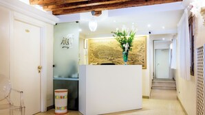 A reception area with a white reception desk, a clear plastic chair, and a decorative vase with flowers. - Hotel Adriatico (Venice)