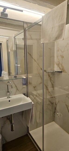 Un baño con ducha acristalada, lavamanos blanco y pared con estampado de mármol.