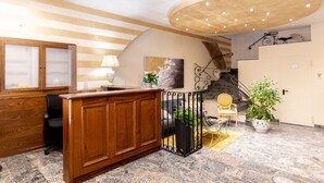A reception area with a wooden desk, a lamp, a painting, a staircase, and a potted plant. - Hotel Corso (Orvieto)