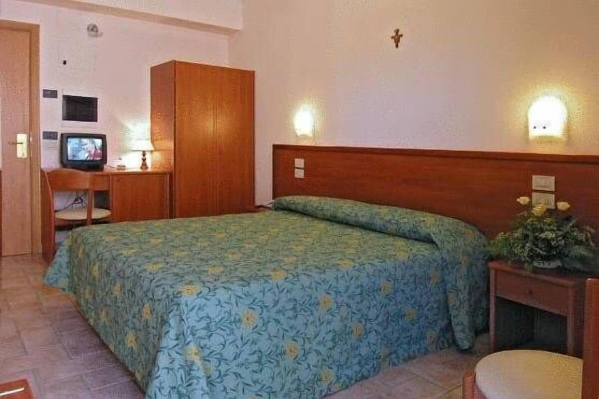 A bedroom with a bed, a desk with a computer, a chair, and a wardrobe.