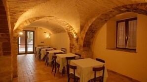 Un comedor con arcos de piedra, mesas con manteles blancos y un ventanal con cortinas.