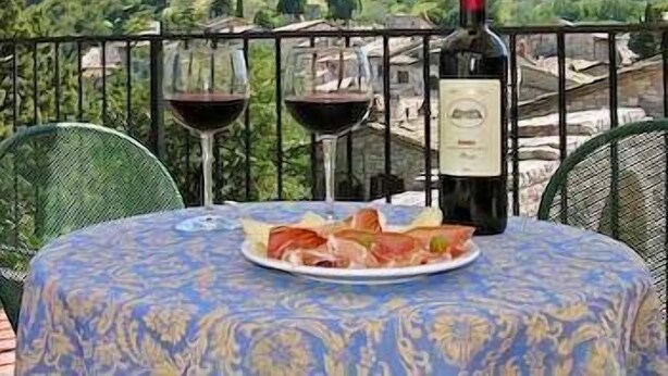 Una mesa con una botella de vino y dos copas, un plato de comida, y una vista panorámica de una montaña y un castillo al fondo.