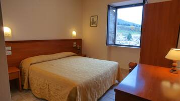 Una camera da letto ordinata con un letto, un comodino e una finestra che offre vista su un paesaggio montuoso.