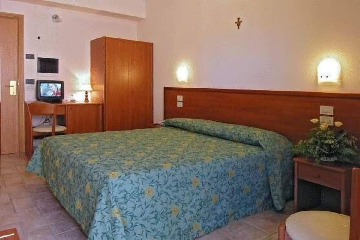 A bedroom with a bed, a wooden wardrobe, a desk with a lamp, and a television.
