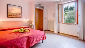 A hotel room with a bed, a window with a view, a radiator, and a door. - Hotel San Rufino (Assisi)