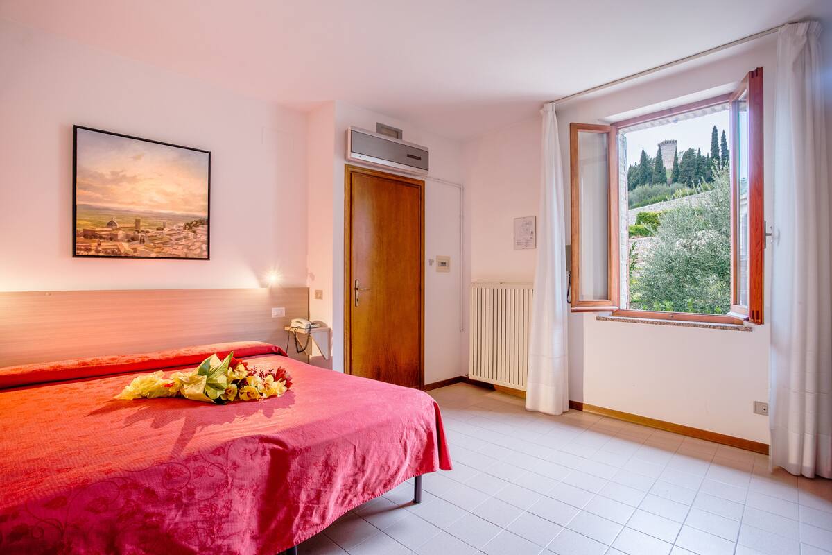 A hotel room with a bed, a window with a view, a radiator, and a door.