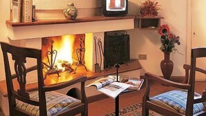 A cozy living room with a fireplace, wooden chairs, a television, and a bookshelf. - Hotel San Rufino (Assisi)