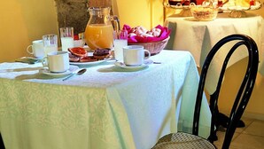 A breakfast setting with a table set for two, including a pitcher of orange juice, pastries, and a vase of red flowers. - Hotel San Rufino (Assisi)