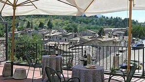 An outdoor terrace with tables and chairs, overlooking a village. - Hotel San Rufino (Assisi)