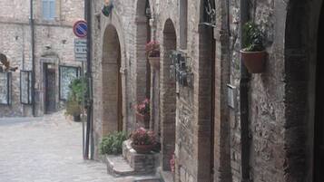 Una stretta strada acciottolata con edifici in pietra, portali ad arco e fioriere pensili.