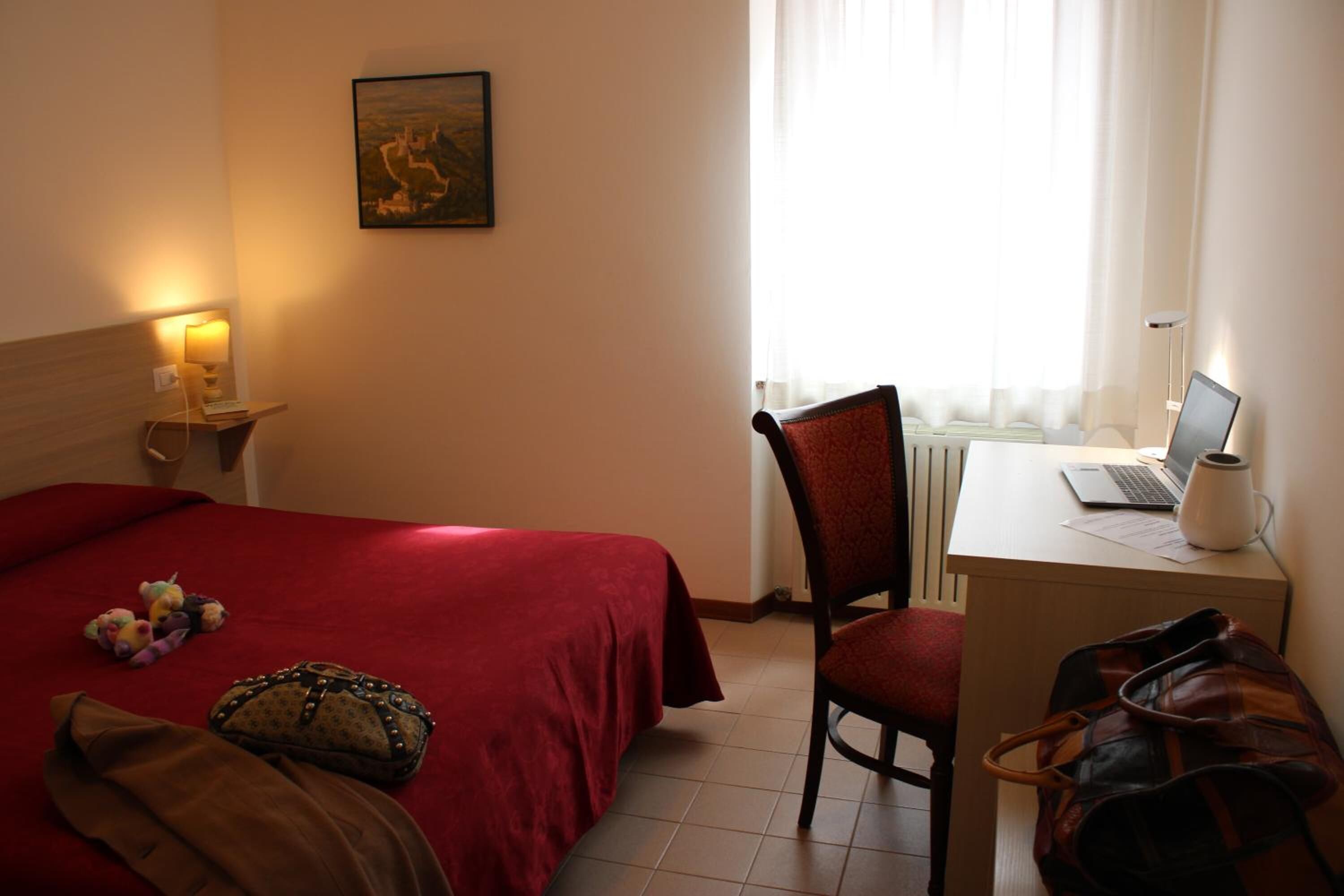 Una habitación de hotel con una cama, un escritorio con una computadora portátil, una silla y una ventana con cortinas.