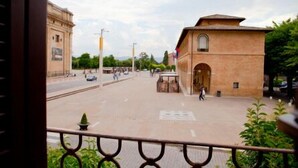 A view of a building with a large open plaza in front, a flagpole, and a person walking. - Porziuncola (Assisi)