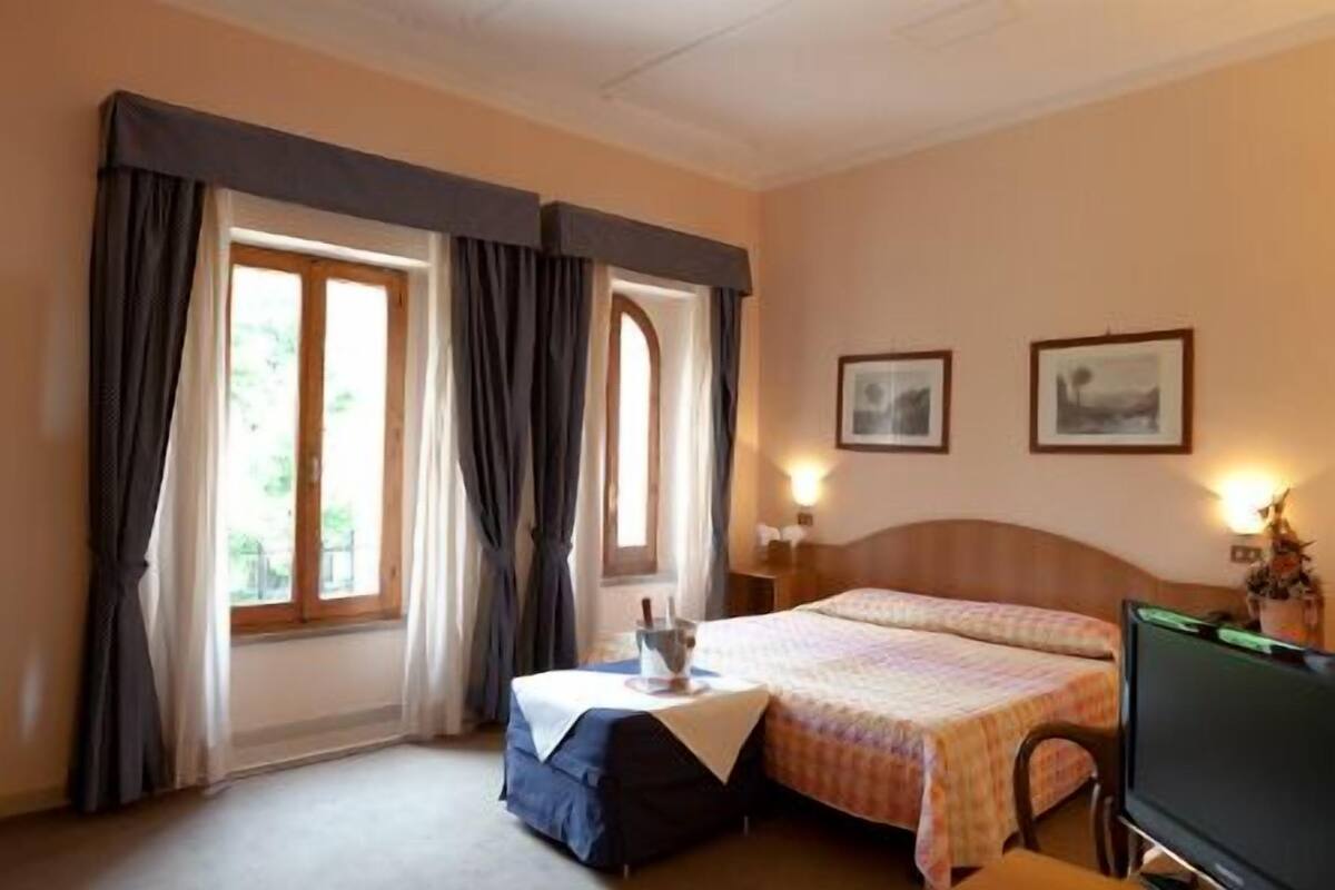 Ein Hotelzimmer mit zwei Betten, einem Fernseher, einem Schreibtisch mit Lampe und zwei gerahmten Bildern an der Wand.