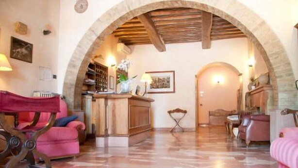 A spacious living area with a wooden reception desk, a pink sofa, and a patterned floor. - Porziuncola (Assisi)