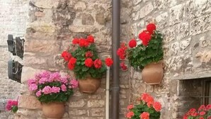 A stone building with flower planters on the wall, two metal chairs, and a small round table. - Hotel San Giacomo (Assisi)