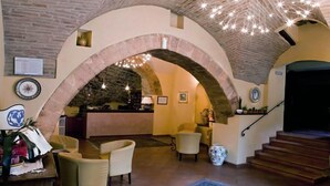 A spacious lobby with a high arched stone ceiling, a reception desk, comfortable seating, and a staircase leading to upper floors. - Hotel San Giacomo (Assisi)