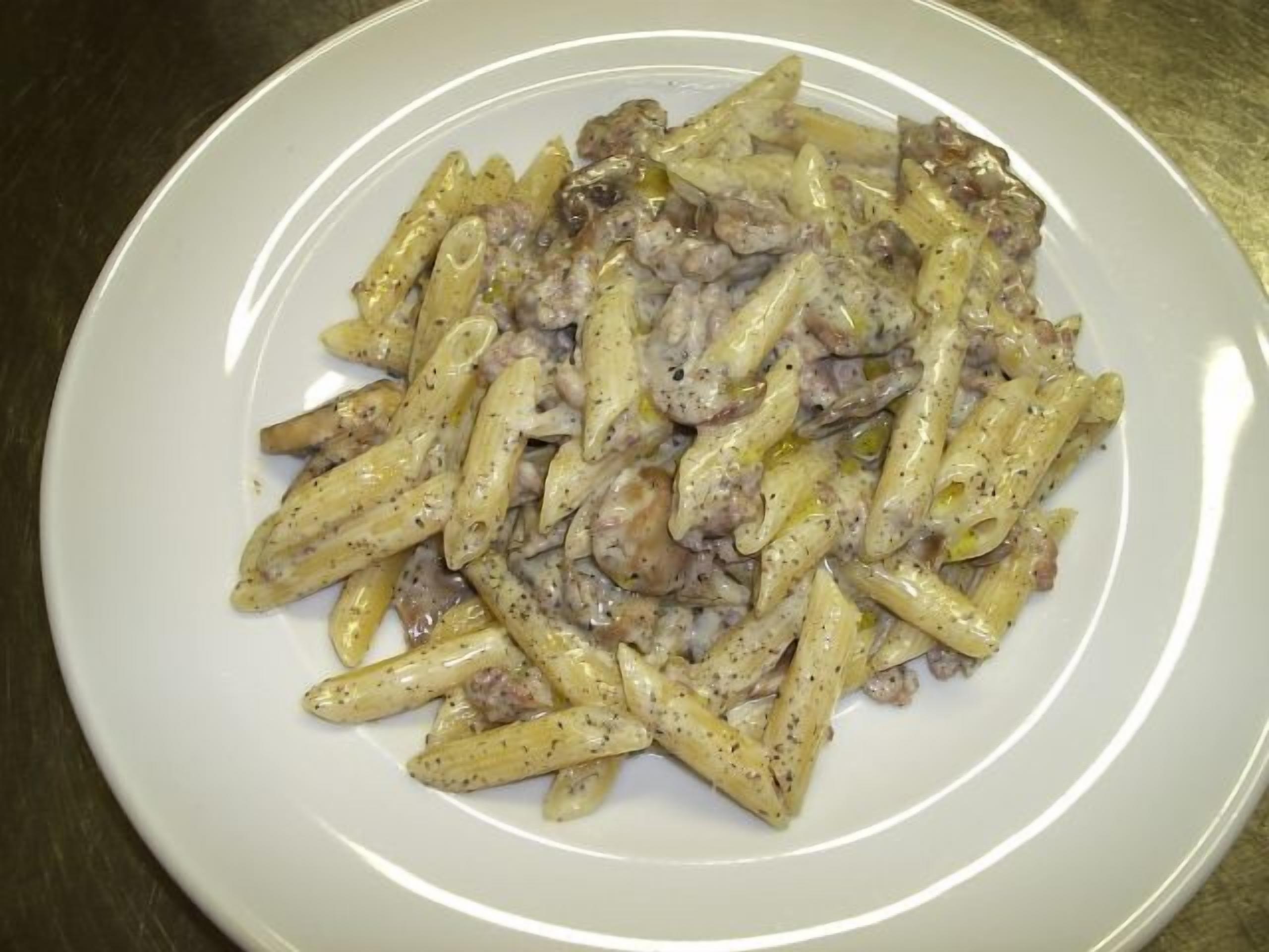 Een bord penne pasta met een romige saus en champignons.