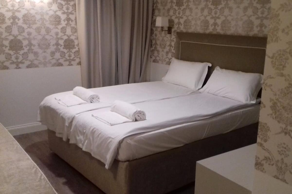 A neatly made bed with white linens and two rolled towels, a headboard, and floral wallpaper.