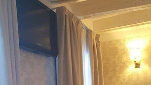 A room with a bedside table, a lamp, a wall-mounted light, and a window with curtains. - Hotel Bartolomeo (Venice)