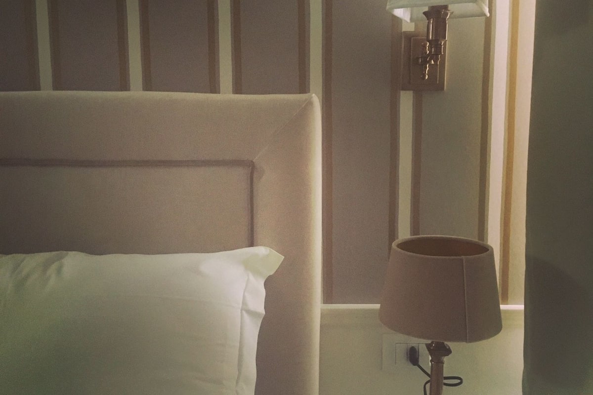 A bed with a white pillow and a nightstand with a lamp.
