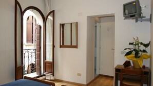 A bedroom with a bed, a desk, a chair, a TV, and a plant. - Hotel Caprera (Venice)