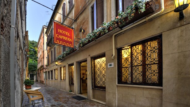 A narrow cobblestone street with a hotel named "HOTEL CAPERRERA" on the right. - Hotel Caprera (Venice)