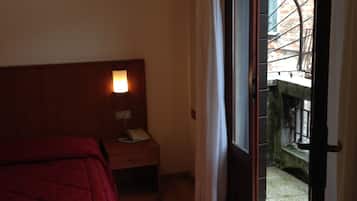 Una camera d'albergo con un letto, un comodino, una lampada e una porta scorrevole in vetro che dà su uno spazio all'aperto.