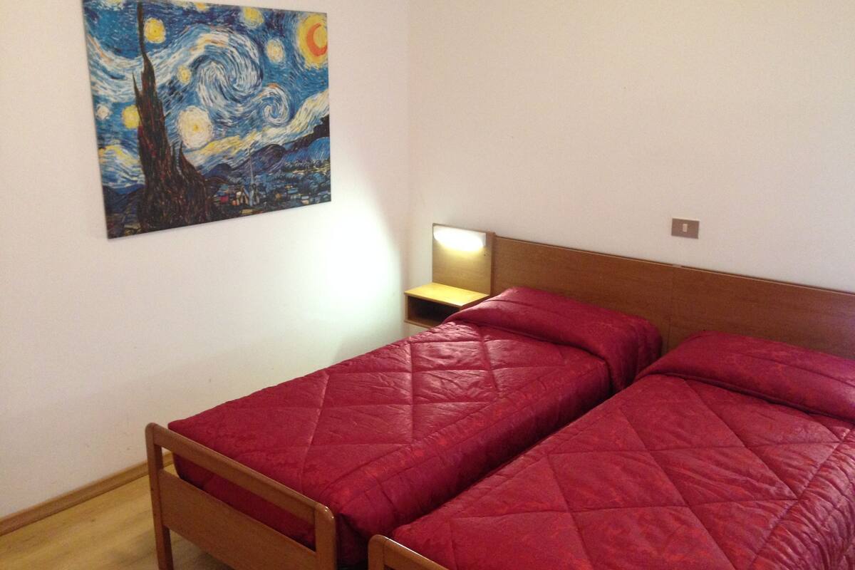 A bedroom with two beds, a wooden headboard, a nightstand, a lamp, and a painting of a starry night on the wall.