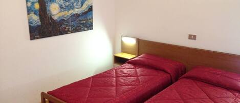 Un dormitorio con dos camas, cabeceros de madera, una mesita de noche, una lámpara y un cuadro de una noche estrellada en la pared.