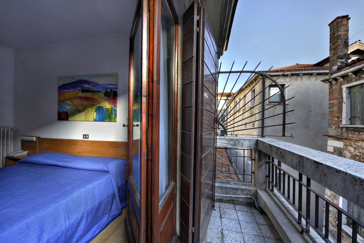 A narrow corridor with a wooden door, a metal railing, and a staircase leading to a balcony.