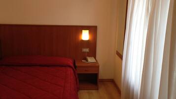 A hotel room with a wooden bed, a nightstand with a lamp, and a window with curtains.