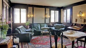 Una habitación con paneles de madera oscura, sofás de cuero verde, un tapete estampado y una mesita con mantel blanco.
