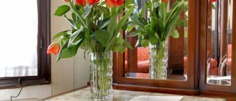 Un bureau en bois avec un miroir, deux vases en verre contenant des fleurs rouges et une chaise verte.