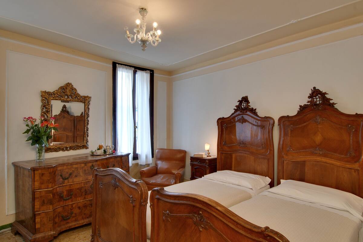 Una camera da letto con un letto di legno, una cassettiera, una sedia, uno specchio e un lampadario.