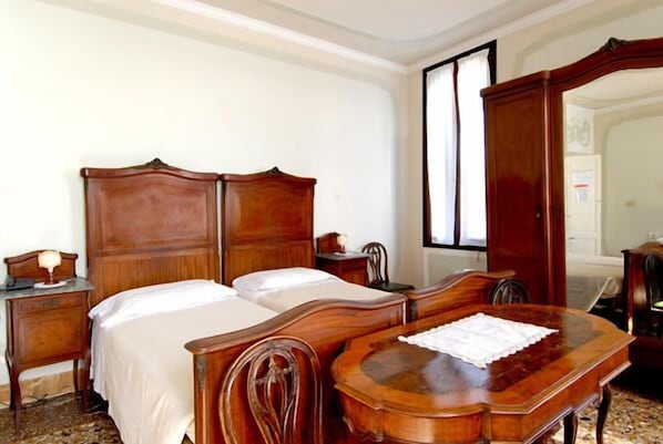 A bedroom with a double bed, a wooden nightstand, a dresser, and a wooden table with a placemat. - Pensione Seguso (Venice)
