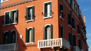 Un edificio rojo con varias ventanas y balcones, un letrero que dice "PENSIONE SEGVSO", y un canal al frente.