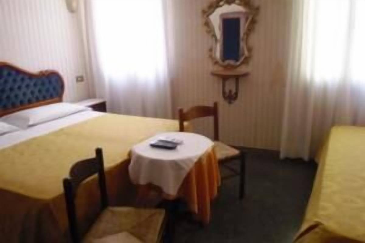 A hotel room with a bed, a small table with a chair, and a mirror on the wall.