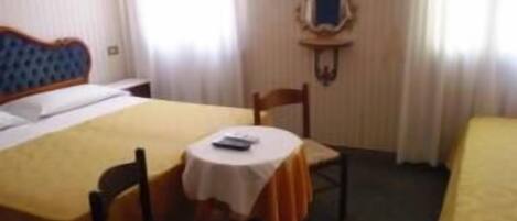 A hotel room with a bed, a small table with a chair, and a mirror on the wall.