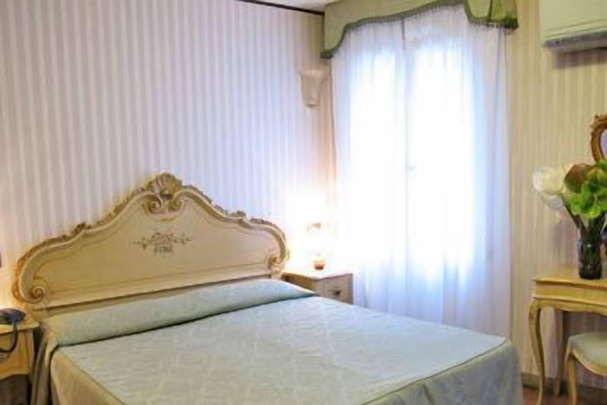 A hotel room with a large bed, a bedside table, a chair, and a window with curtains.