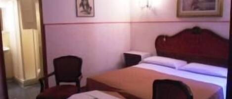 A small, single-bed room with a wooden headboard, a bedside table, and two chairs.