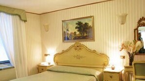 Hotellihuone, jossa on sänky, työpöytä, tuoli, taulu seinällä ja ikkuna, jossa on verhot.
