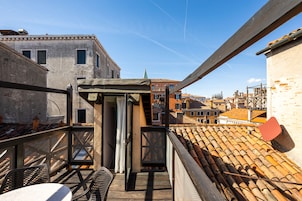 A rooftop terrace with a view of the cityscape, featuring a wooden railing, a small table, and chairs.