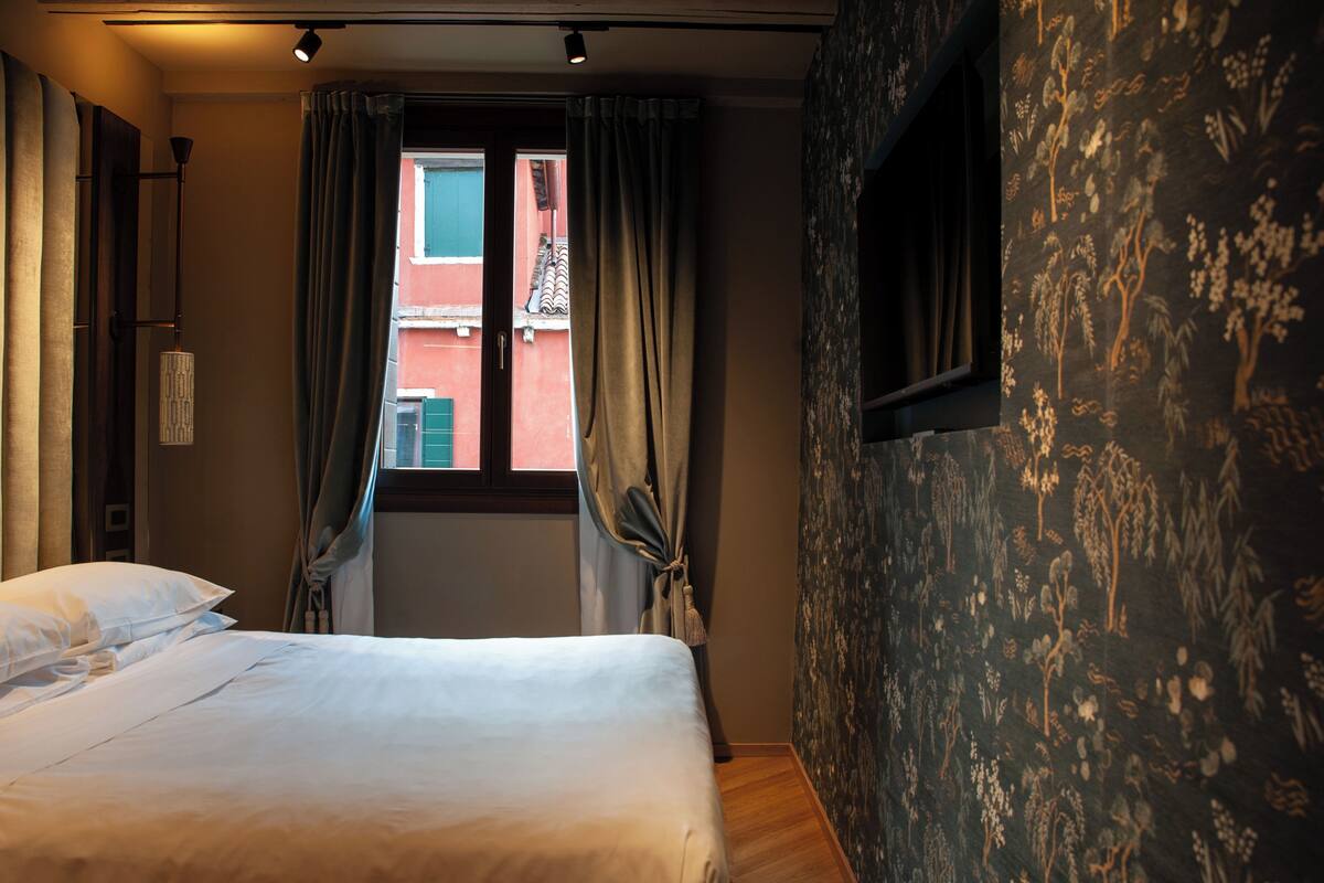 Una habitación de hotel con cama, cortinas, ventana y pared con estampado floral.