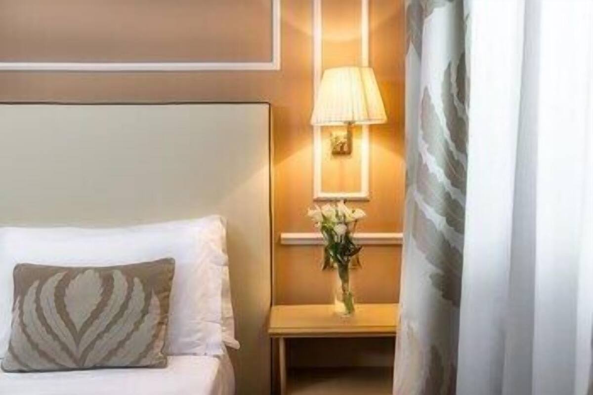 Ein Hotelzimmer mit einem Bett, einem Nachttisch mit Lampe und einer Vase mit Blumen.