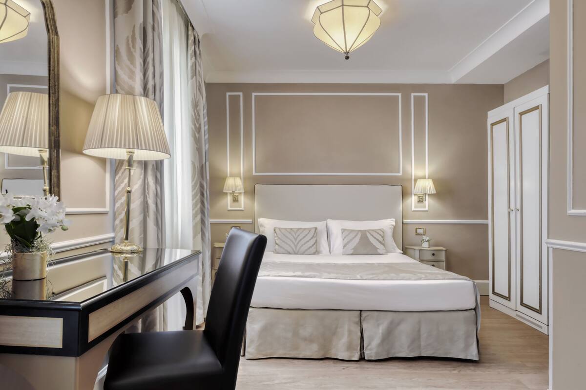 Ein Hotelzimmer mit einem großen Bett, einem Schreibtisch mit Spiegel, einem Stuhl und Nachttischlampen.