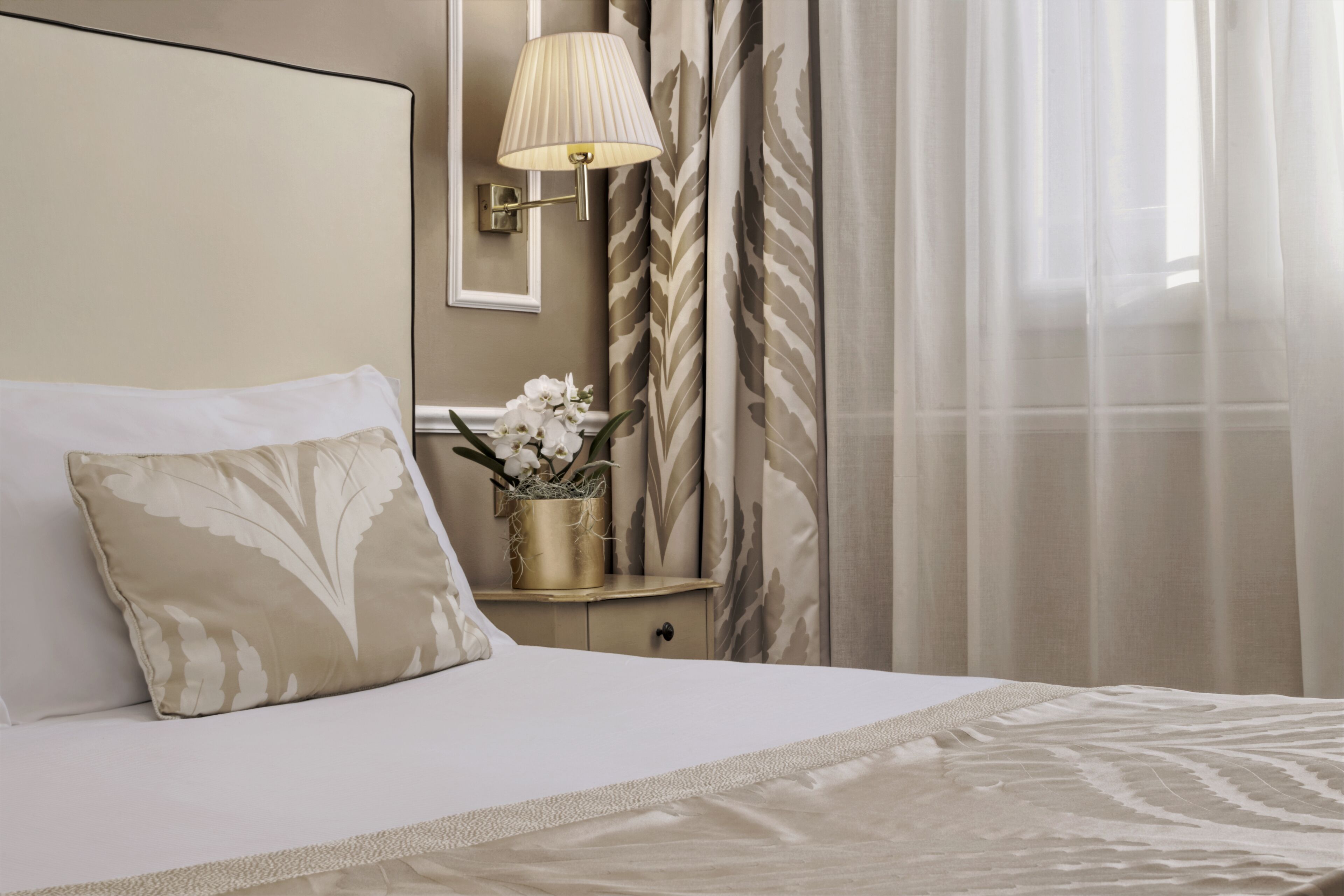 A neatly made bed with a decorative pillow, a bedside table with a lamp, and a vase with flowers.