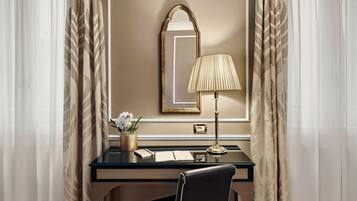 Habitación de hotel con escritorio, silla, lámpara, espejo y un jarrón con flores.