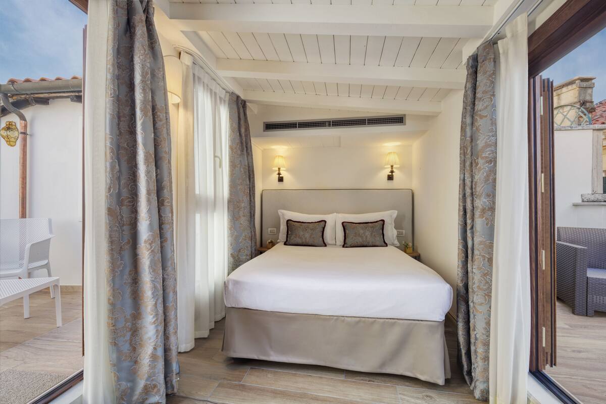 Ein Schlafzimmer mit einem großen Bett, zwei Wandlampen und Blick ins Freie.