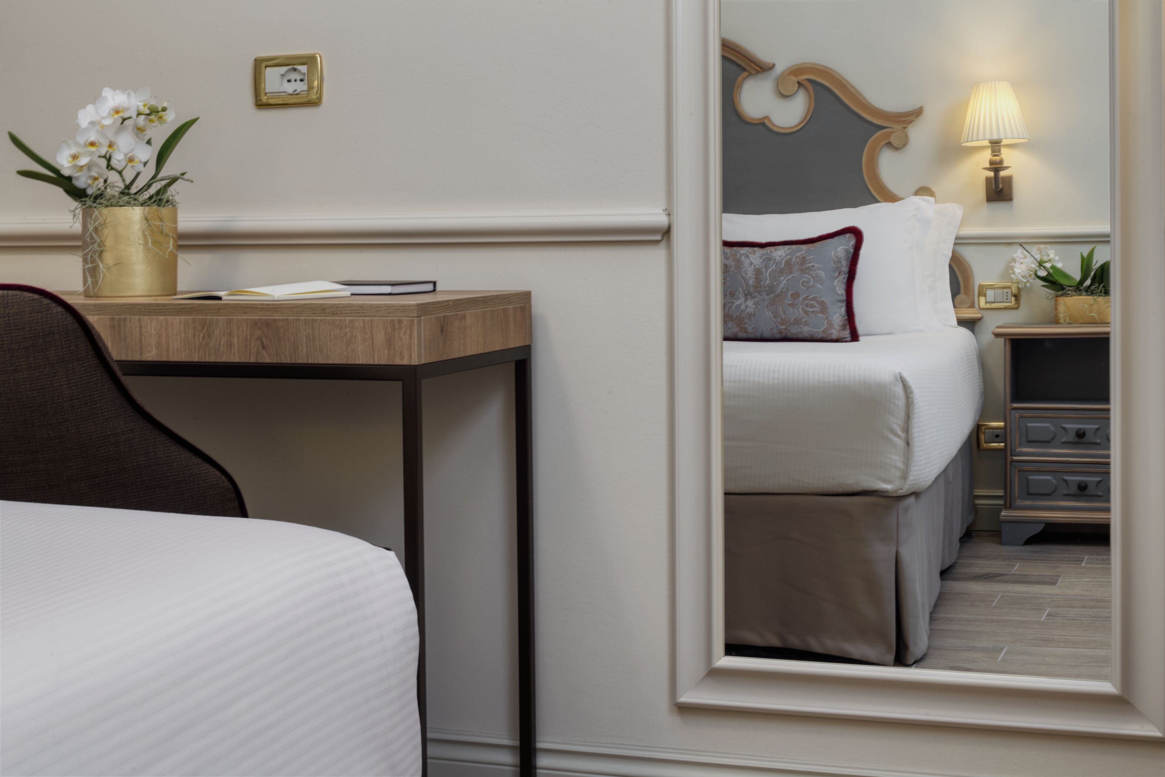 Ein Hotelzimmer mit einem Bett, einem Nachttisch mit Lampe, einer kleinen Pflanze und einem Spiegel, der den Raum reflektiert.