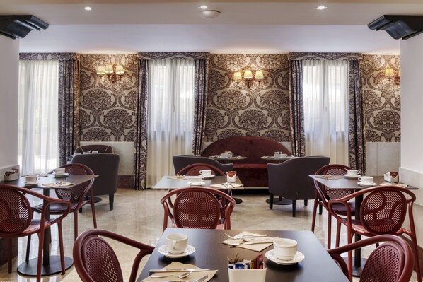 Un comedor con mesas y sillas, papel tapiz estampado y apliques de pared.